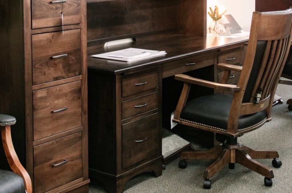 Close up of a hardwood desk, hardwood filing cabinet, and a hardwood office chair with black leather seat cushion.