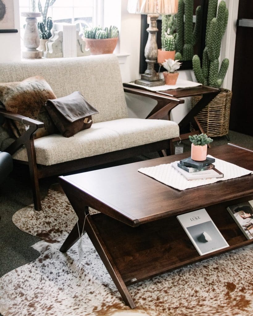 Brown hardwood coffee table and a white sofa on a cowhide rug in a living room decorated with cacti plants.