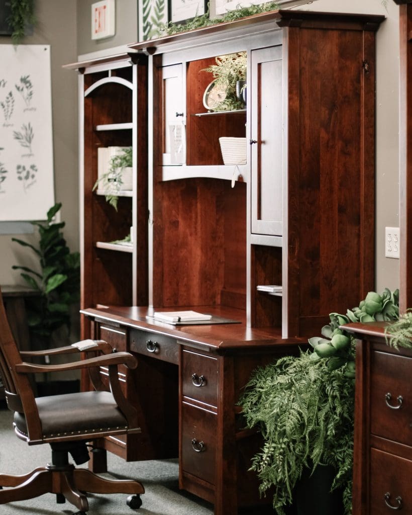 Brown hardwood office desk with hutch top with decorative plants and a black leather office chair.