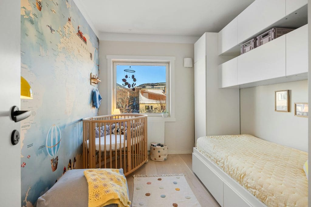 Nursery with white walls, an oval wood crib, a twin bed, and an accent light blue wall with a travel theme.