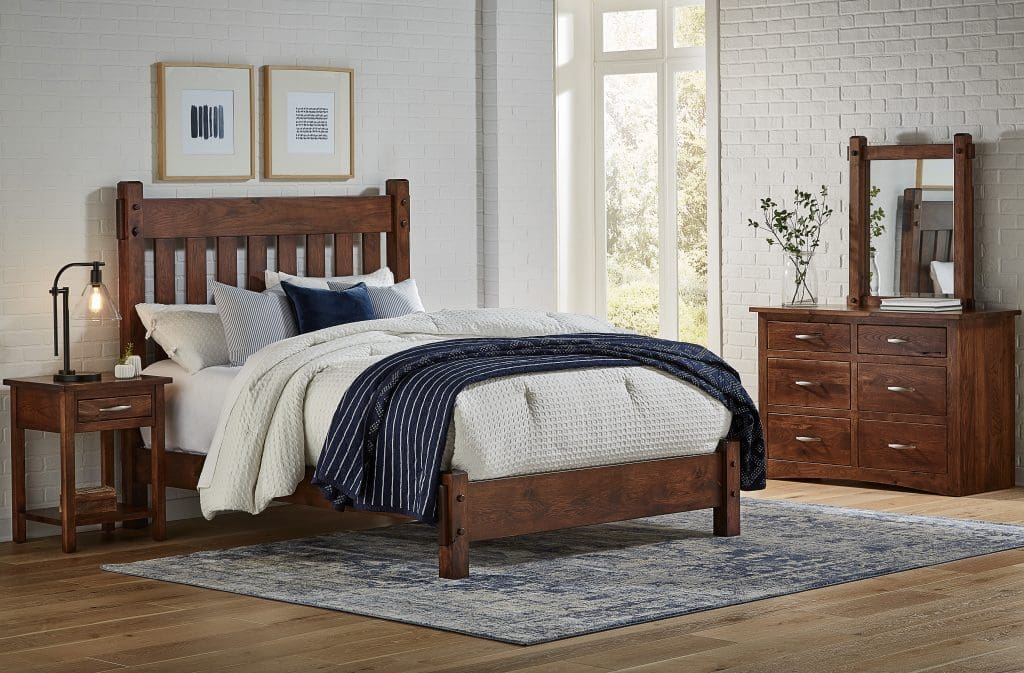 Bedroom with dark brown hardwood bed, nightstand, and dresser in a room with white walls, a blue and white rug, and tan wood plank flooring.
