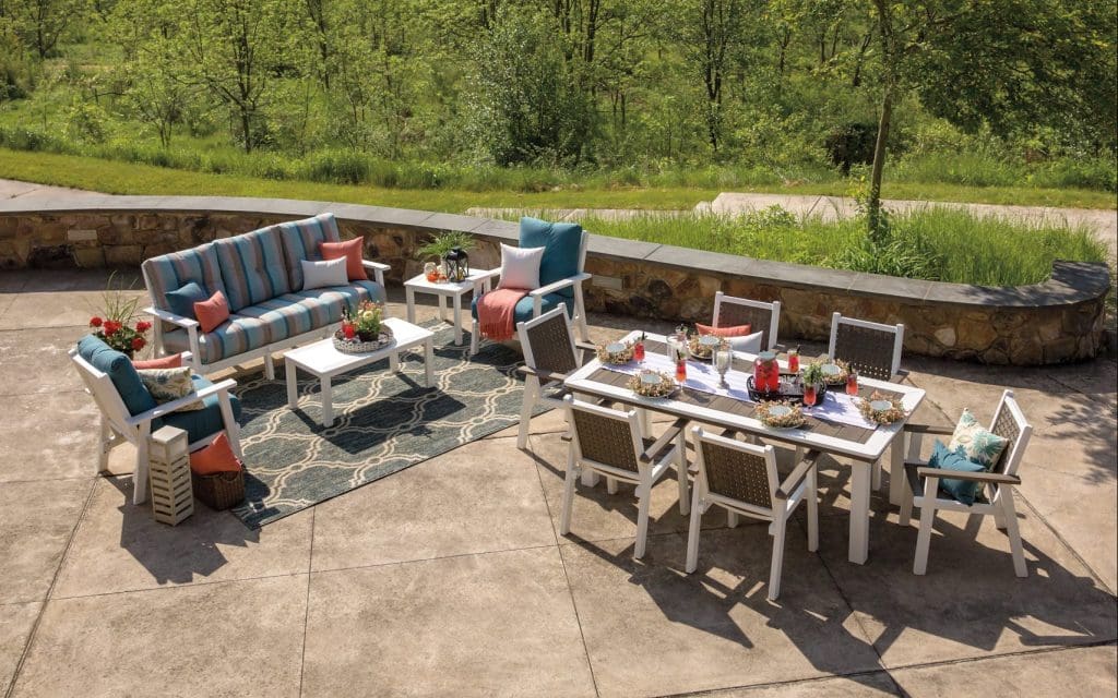 Overhead view of poly lumber furniture on a back stone patio with a brown and white dining set and a blue and white couch set.