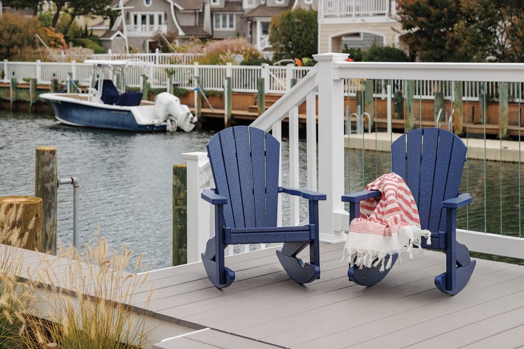 Set of 2 navy blue poly lumber rocking chairs on a deck by a boat marina.
