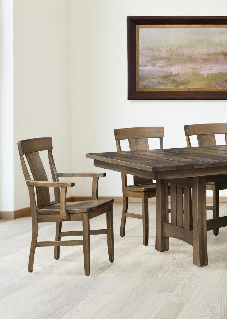 Close up of a dining room table with a rough sawn top and trestle base, with matching hardwood chairs around it. 