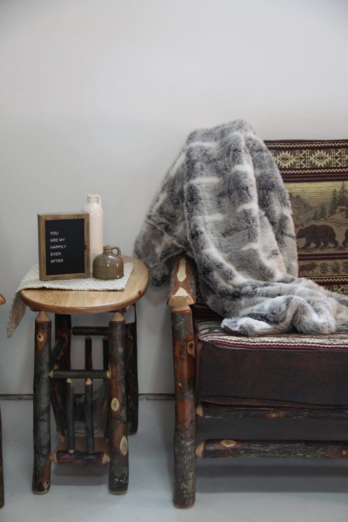 Rustic log trim sofa and end table with a gray and white throw blanket, 2 ceramic vases, and a small wood letterboard.