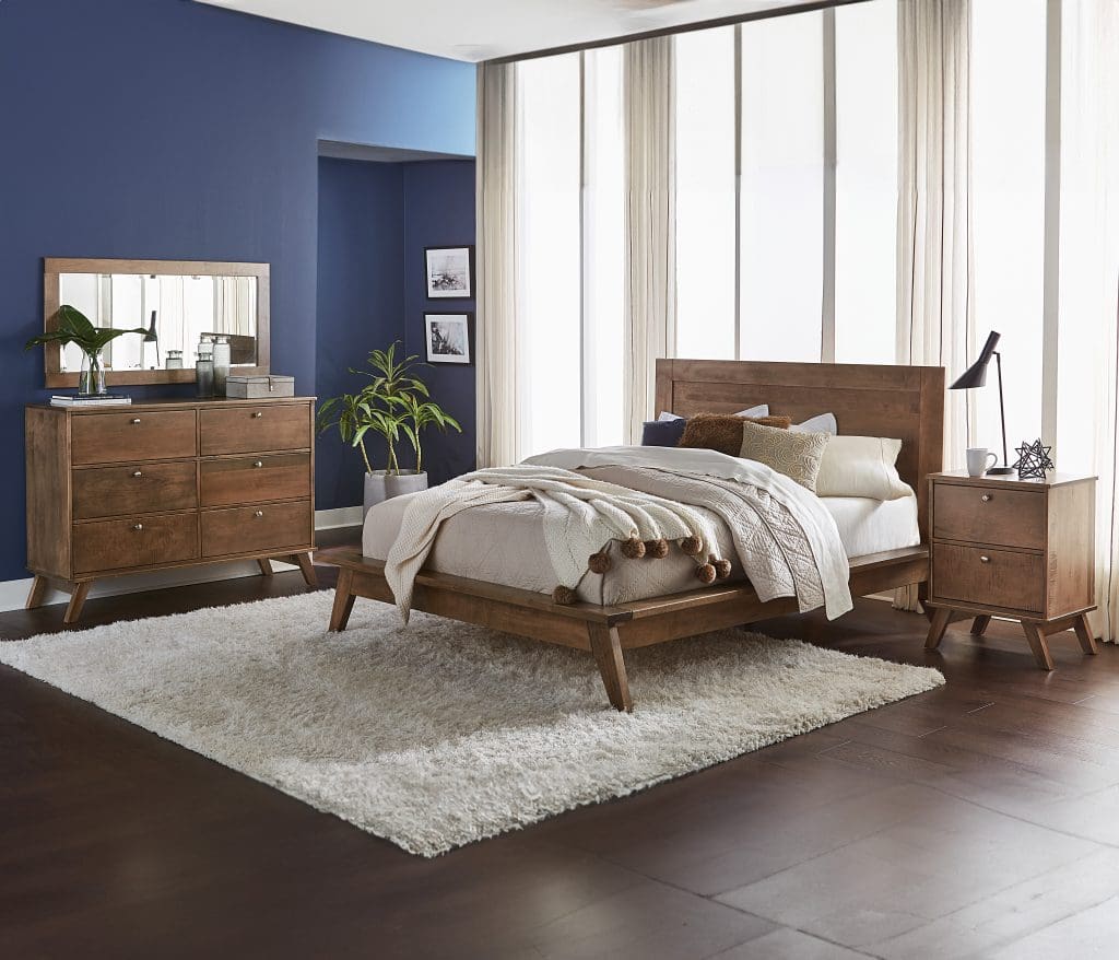 Liberty Bed and bedroom set with brown stained hardwood bed, dresser, and nightstand in a room with hardwood flooring, a large white rug, and a dark blue accent wall.