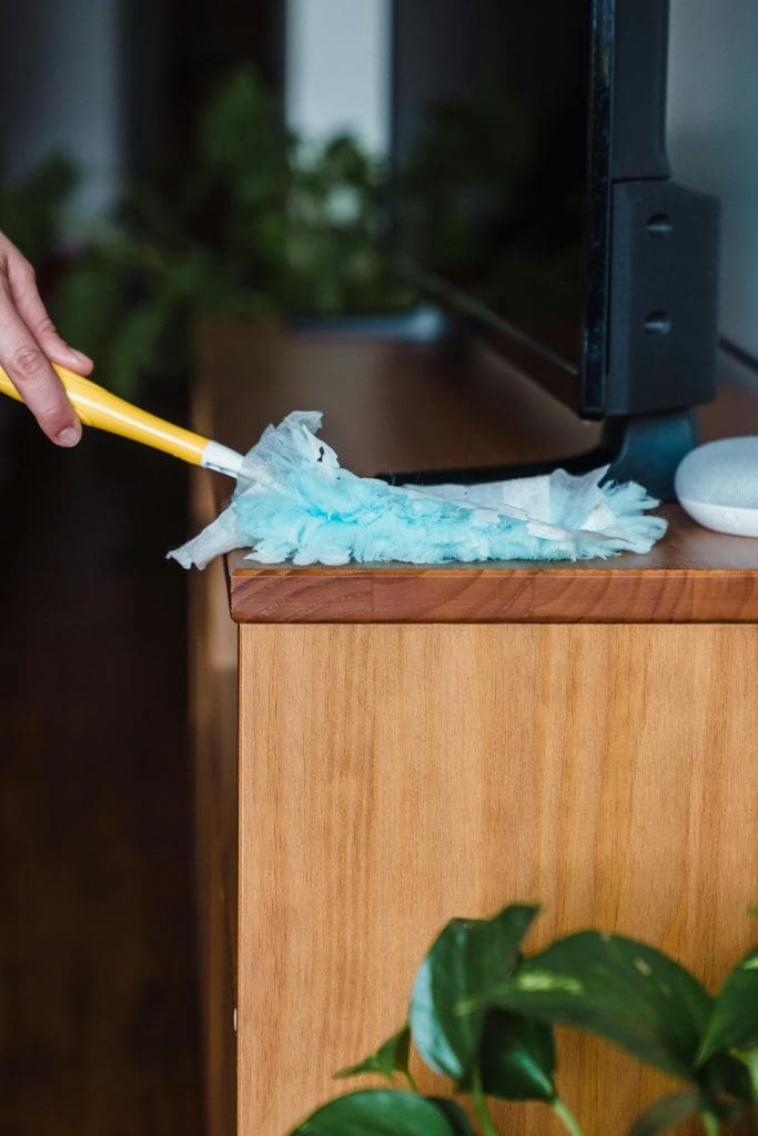 Close up of someone dusting a hardwood TV stand with a black TV on it.