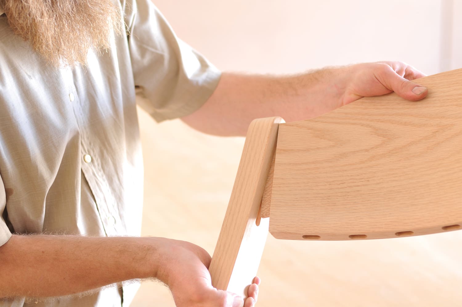 Photo of a man assembling a chair, featuring detailed joinery and wood. 