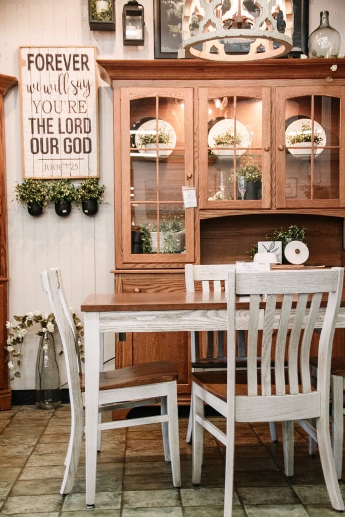 A Dining room with white walls and laminate floors. With a quality oak hutch decorated with black and white accents. In front there is a kitchen table with a white base and a stained top. 