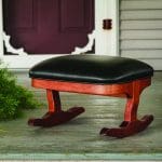 Rocking Tommy Footstool with a stained hardwood base and black leather upholstery.