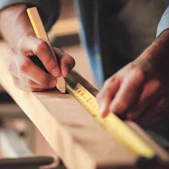 Image of a man of unknown age marking a measurement on a board. Horizontal shot