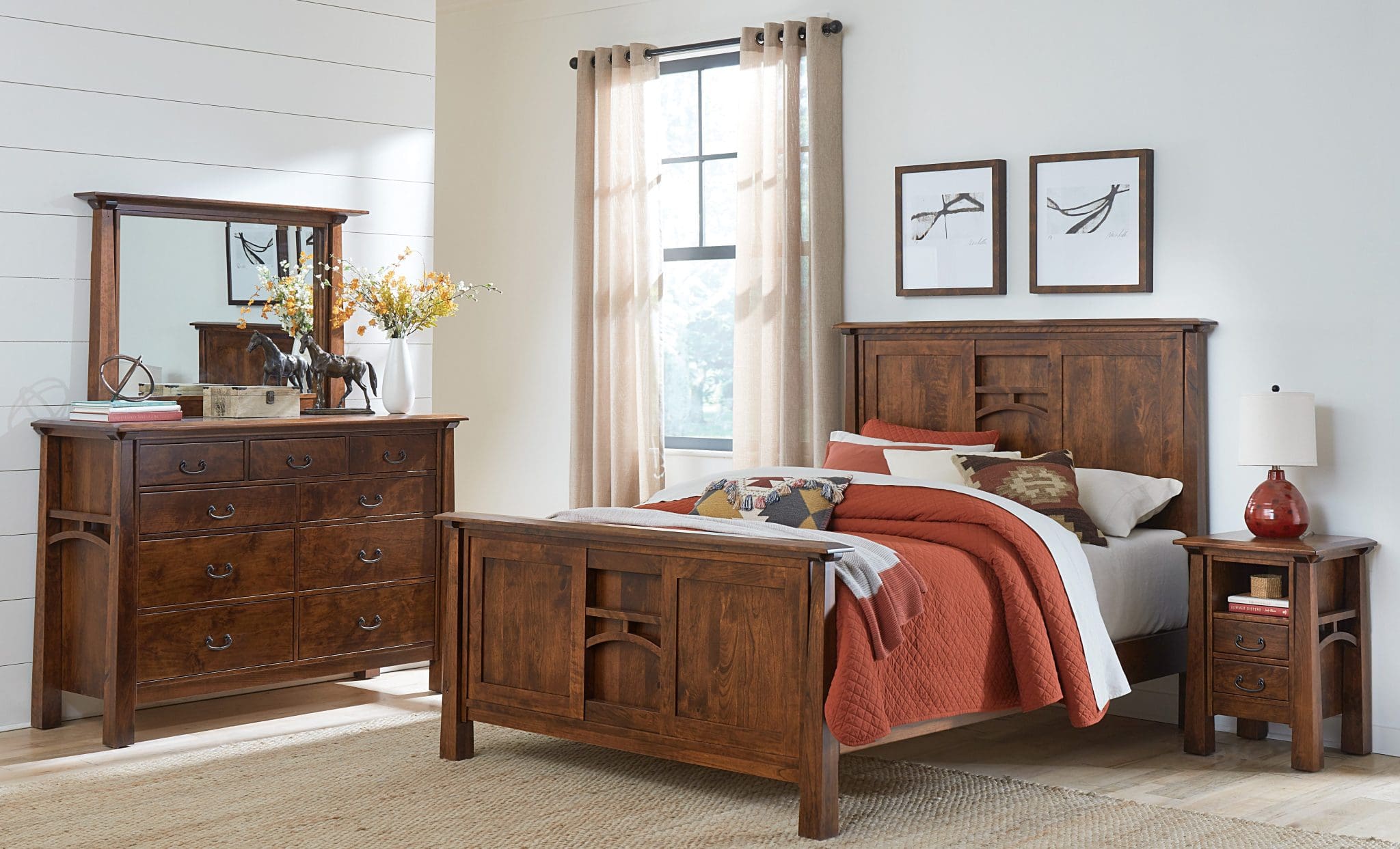 Bedroom with a brown hardwood bed frame with rust and white colored bedding, a brown hardwood standing dresser with a mirror, white walls, tan carpet, and a window with beige curtains.