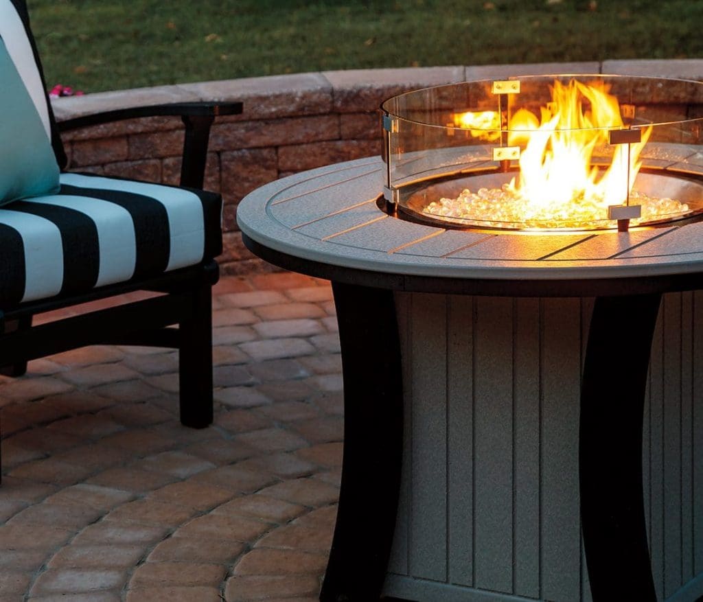 Close up of a round tan and black firetable lit in the center of a patio.