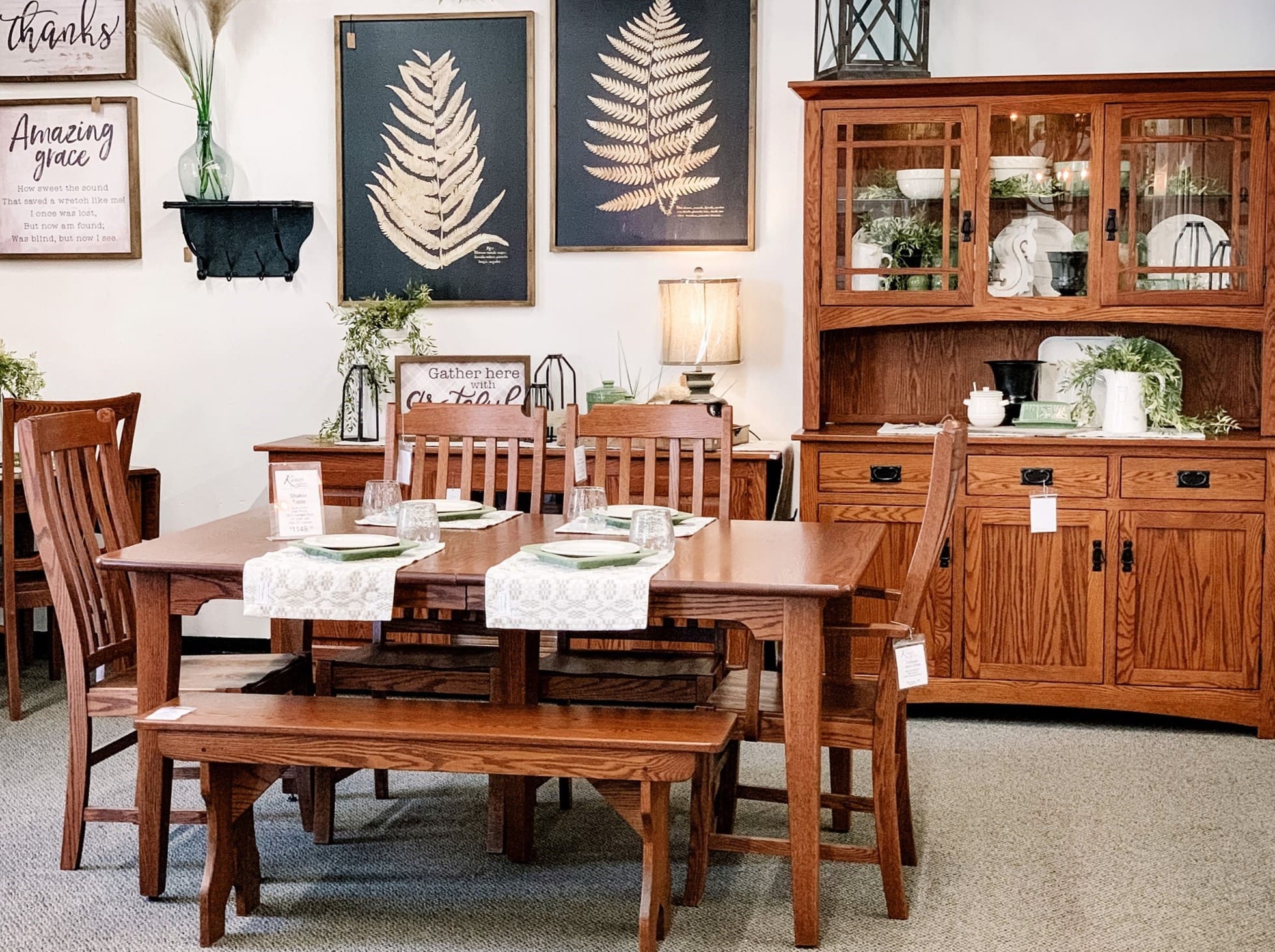 Dining room display set up in King's Impressions' store with a wood dining table set, a 2-door wood dining hutch, 2 large leaf art prints, and rustic decor.